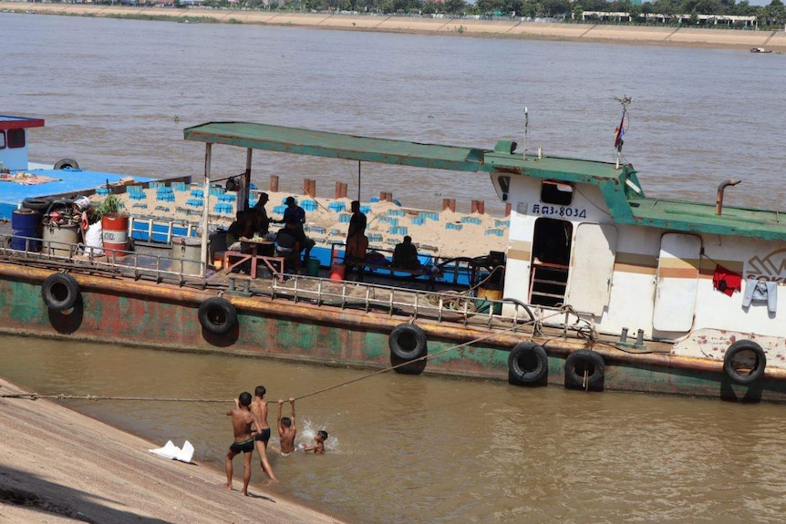 Cambodian children swim beside a large boat
