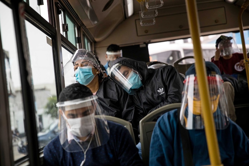Sleeping-looking commuters wearing heavy protective face gear sit on a bus on a dreary day.