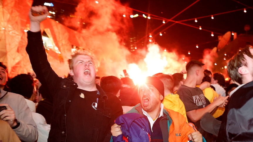 Fans celebrate wildly while flares are lit in the background
