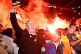 Fans celebrate wildly while flares are lit in the background