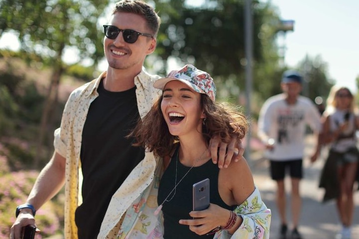 A man holds a woman's shoulder as they walk on the footpath together.