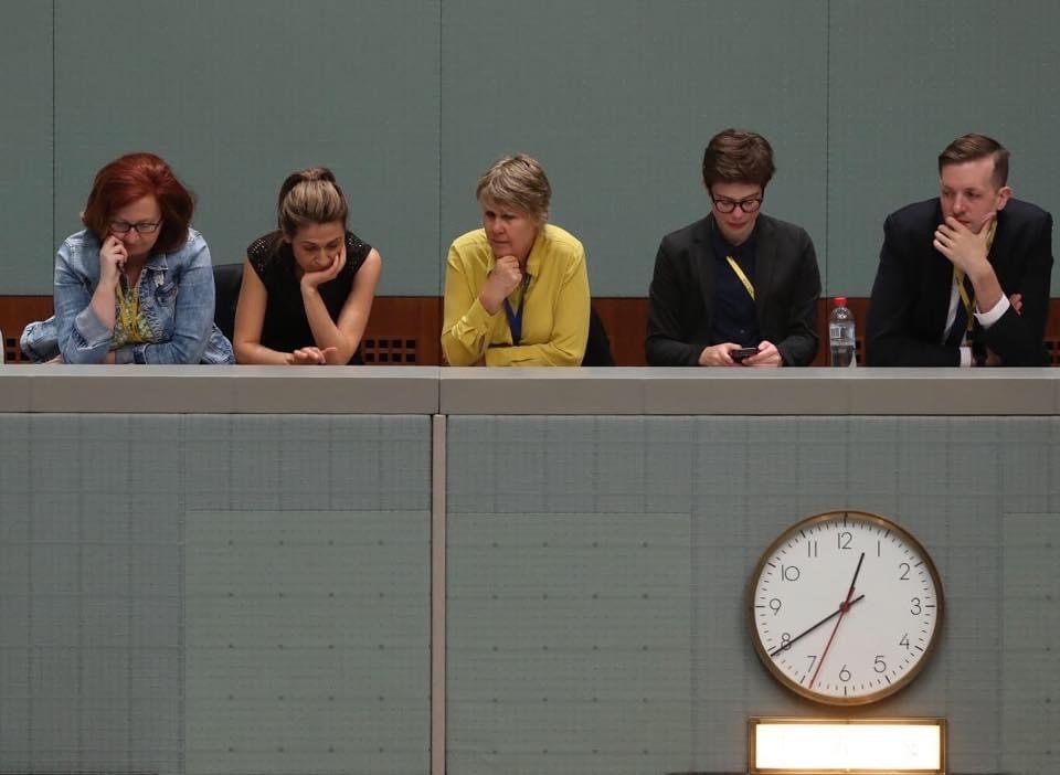 Five people sitting at a bench with a clock underneath them