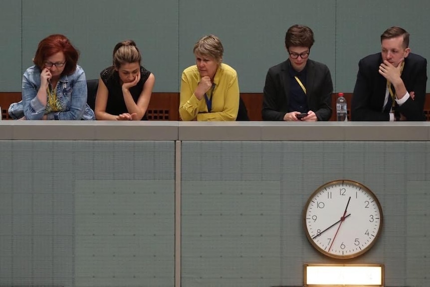 Five people sitting at a bench with a clock underneath them