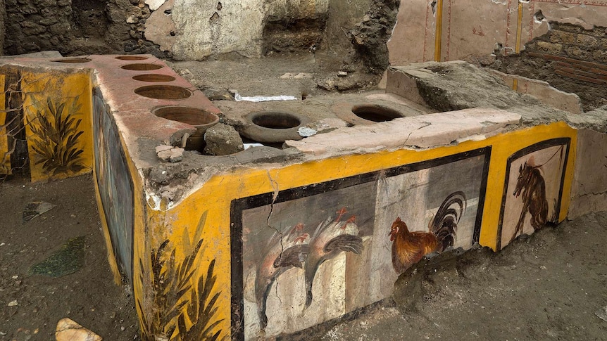 An ancient stone stove with images of roosters and horses stands in front of a crumbling wall.