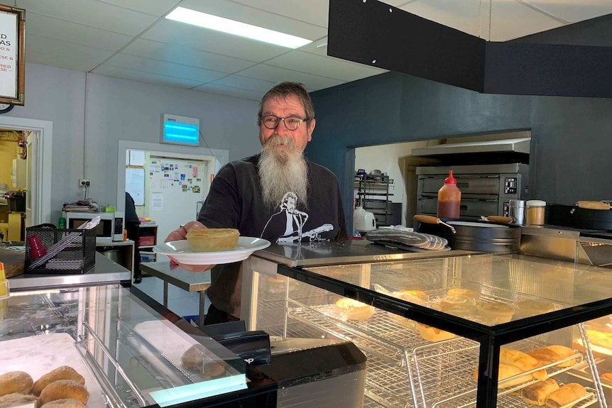 Man stands behind bakery counter holding a plate with a pie