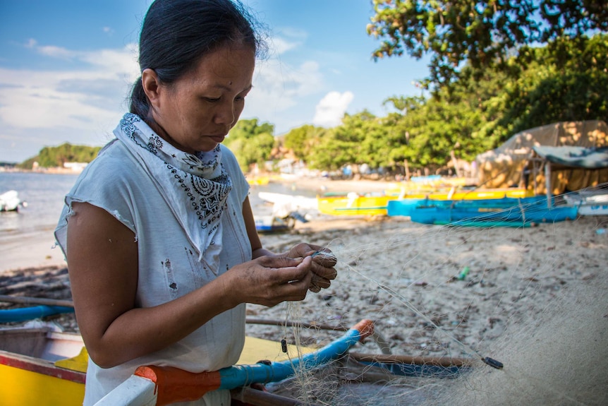 A local fisherwoman at Bolinao untangles fishing nets on the beach.