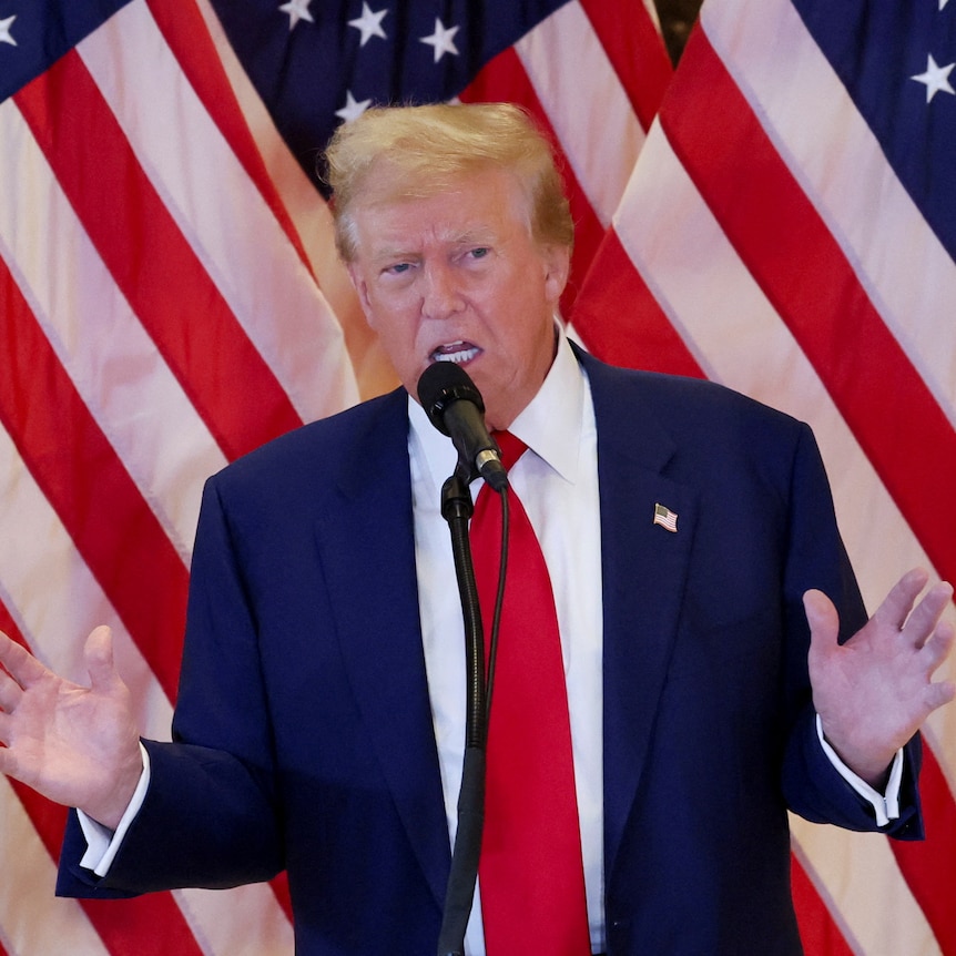 Donald Trump speaks at a press conference with american flags behind him.