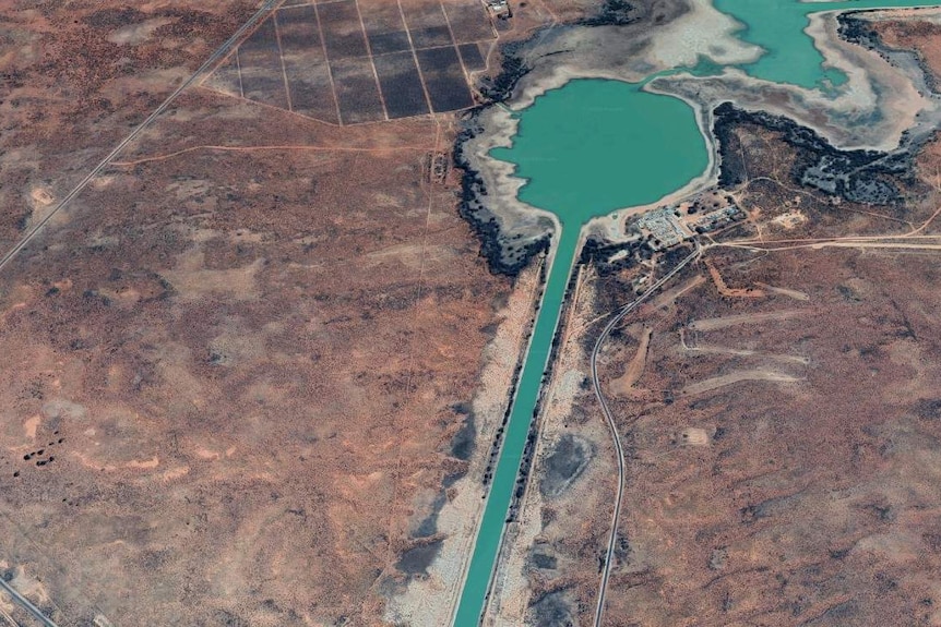 A satellite image of a bright green lake set in a red and brown landscape.