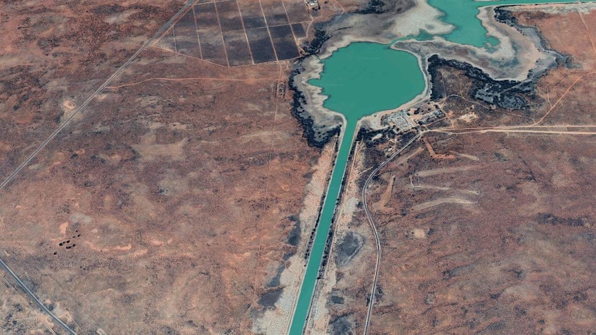 A satellite image of a bright green lake set in a red and brown landscape.