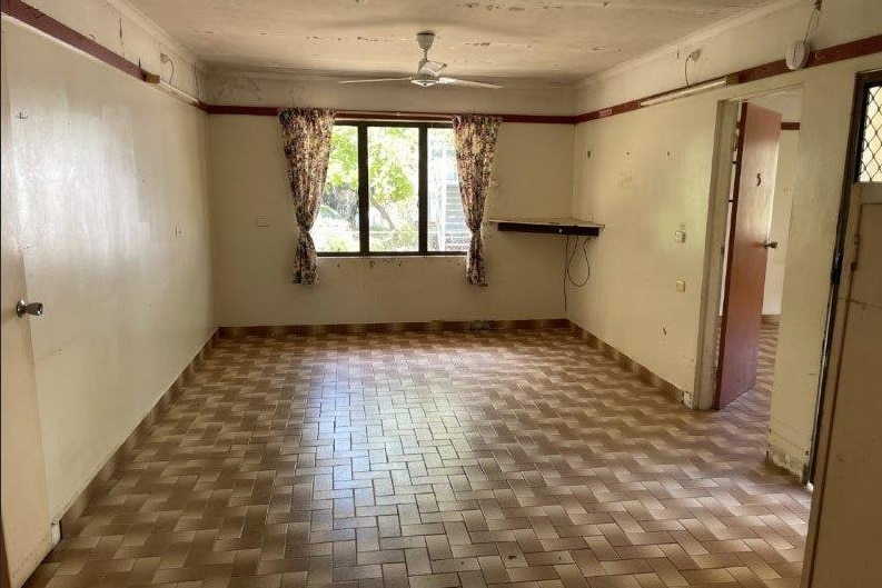 Inside a empty living room with aged tiles and curtains