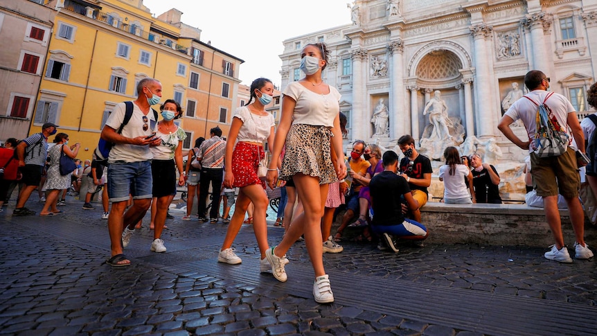 A group of people in face masks walking past the Trevi Fountain
