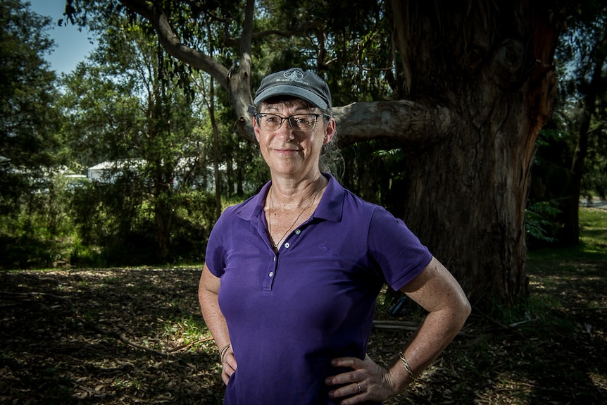 A woman stands underneath a large eucalypt tree.