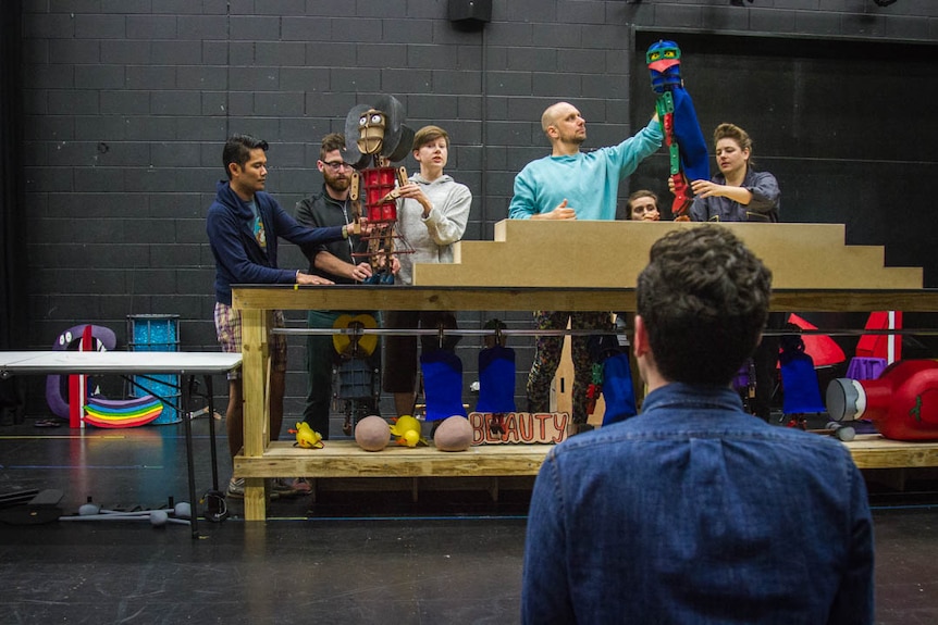 Puppets on a make shift stage rehearse with director.
