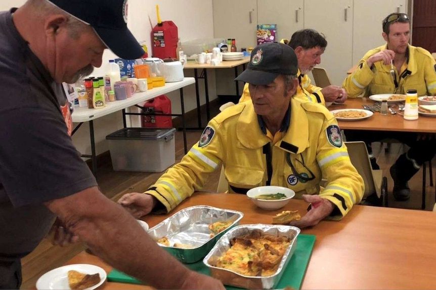 A man serves dinner to a group of firefighters.