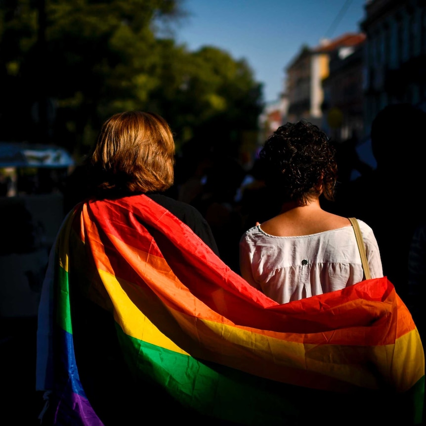 A couple wrapped in rainbow flag taking part in gay pride march.