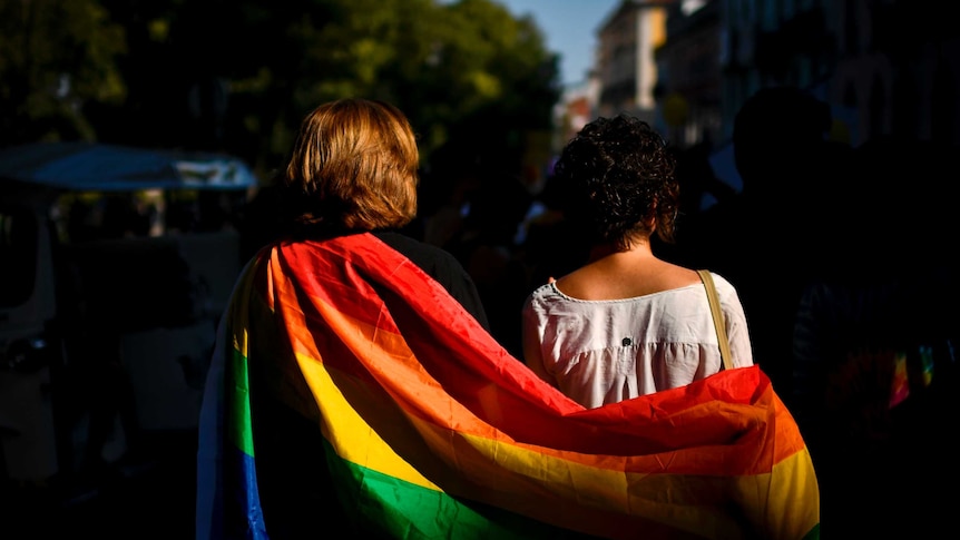 A couple wrapped in rainbow flag taking part in gay pride march.