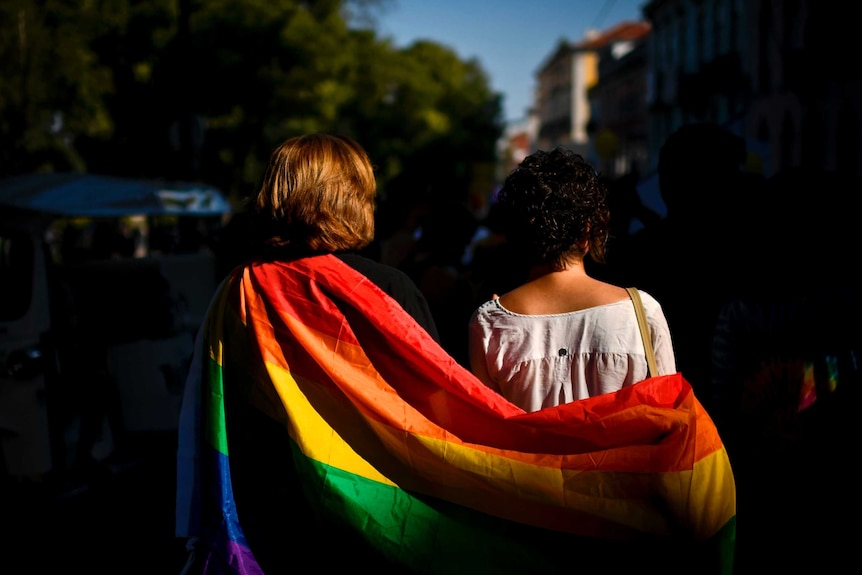 A couple wrapped in rainbow flag taking part in gay pride march.