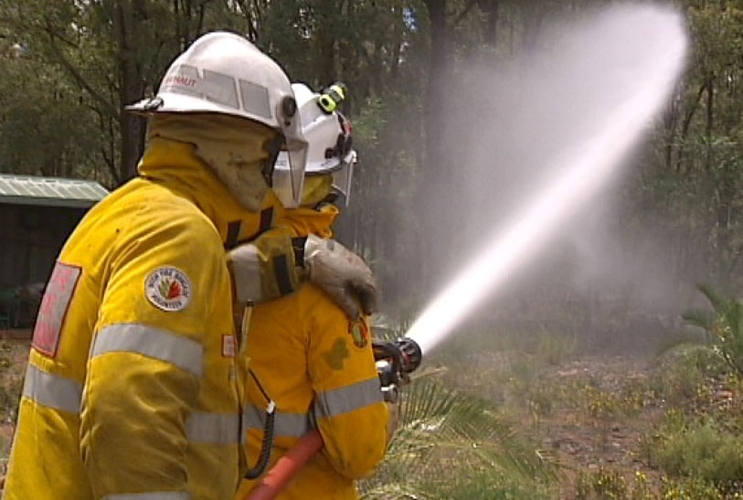Volunteer fire fighters spray water hose in demonstration for Bushfire Awareness Week.