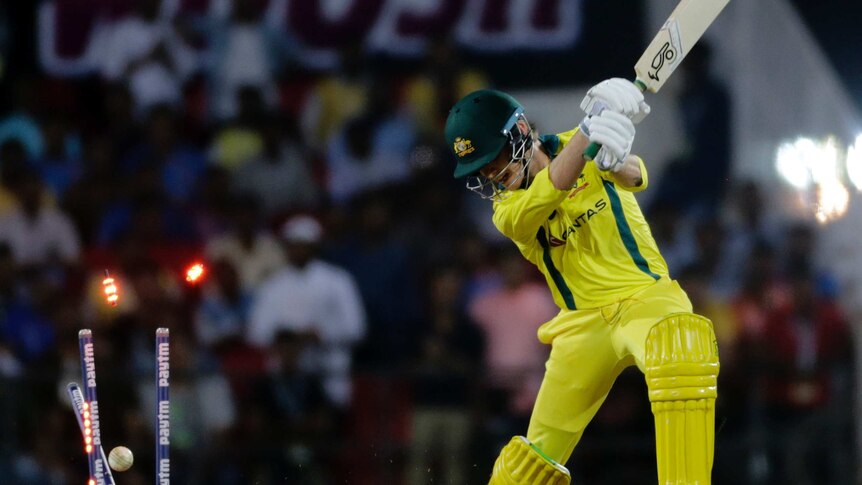 A batsman swings his bat and the bails light up as the ball crashes into the stumps.