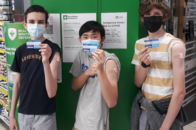 Three teens, Wesly, Darcy and Jack are wearing masks and have their sleeves rolled up showing their vaccination mark.