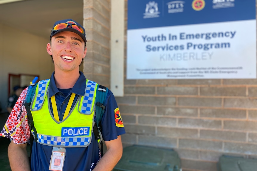 A teenage boy standing in front of a Youth in Emergency Services sign, with a police uniform