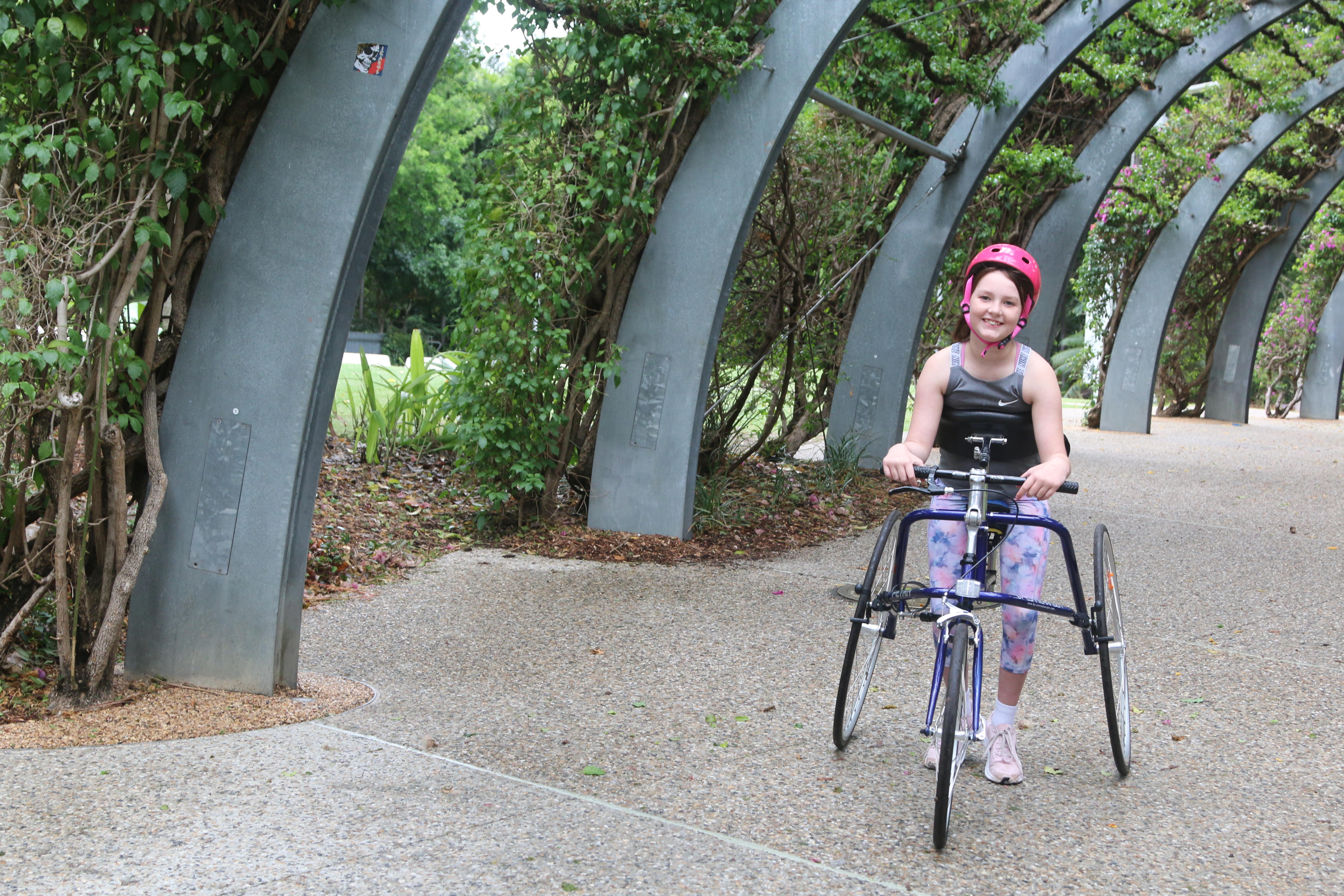 Scarlett Halliday smiles while moving along a path in a three-wheeled frame