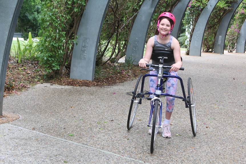 Scarlett Halliday smiles while moving along a path in a three-wheeled frame
