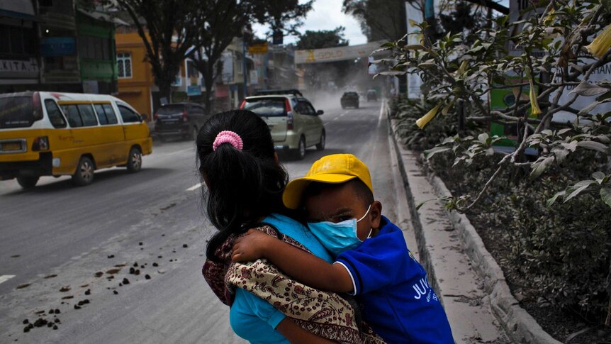 A boy wearing a mask is carried through through an area covered by ash after Mount Sinabung erupted.