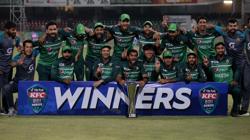 A group of Pakistan cricketers pose with a silver trophy behind a banner saying "Winners".