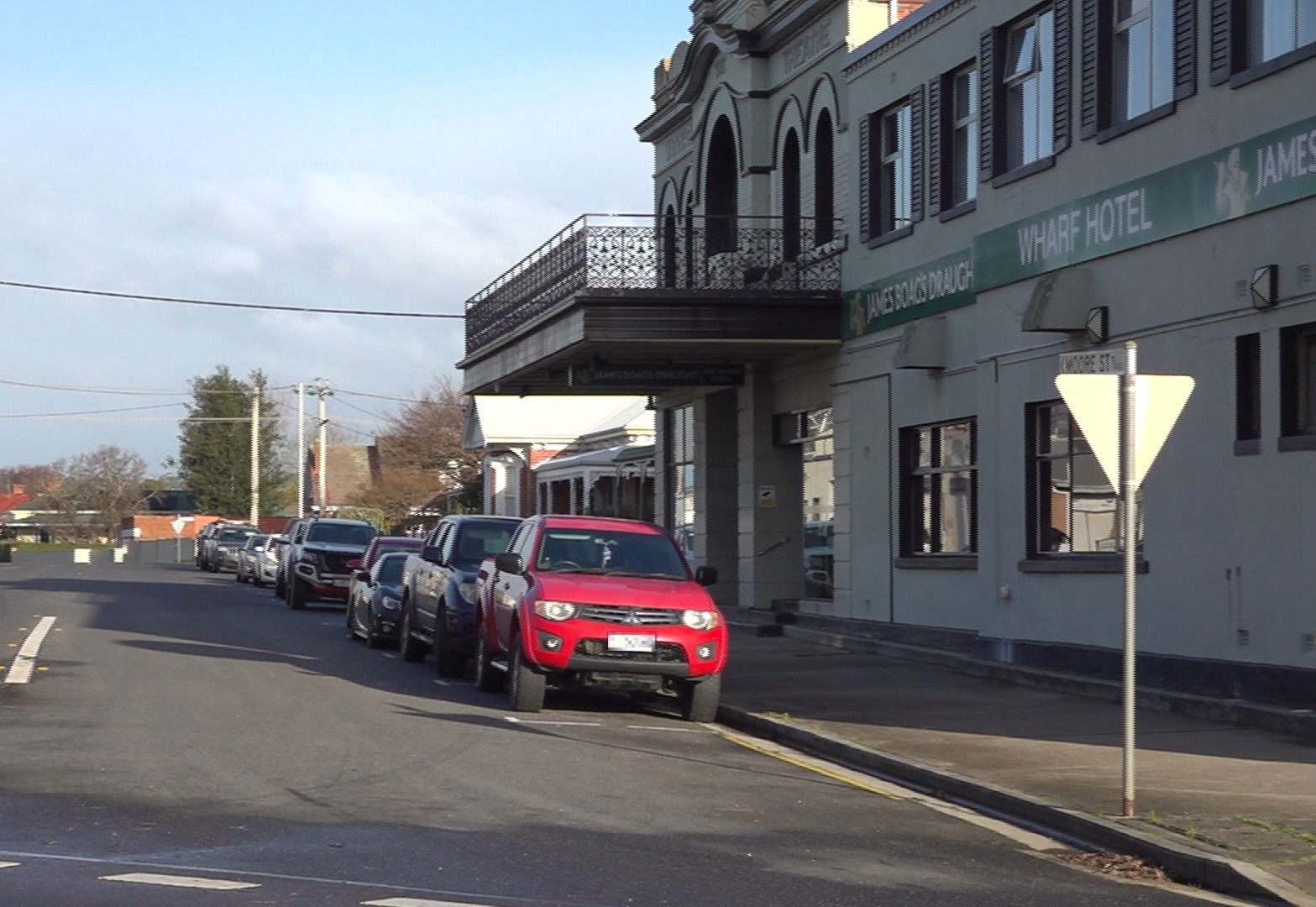 A line of cars parked outside the Wharf Hotel on a sunny day.