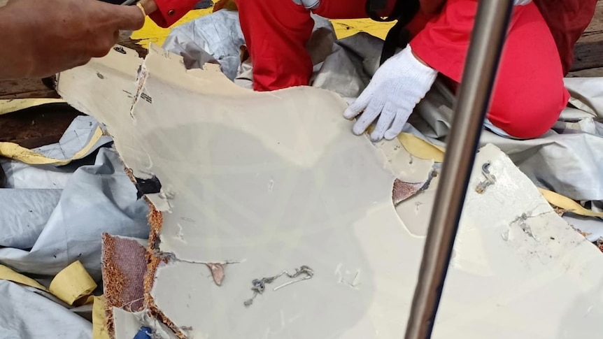 A piece of reported plane wreckage is being held by a man wearing a white glove