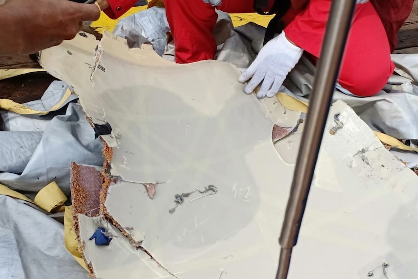 A piece of reported plane wreckage is being held by a man wearing a white glove