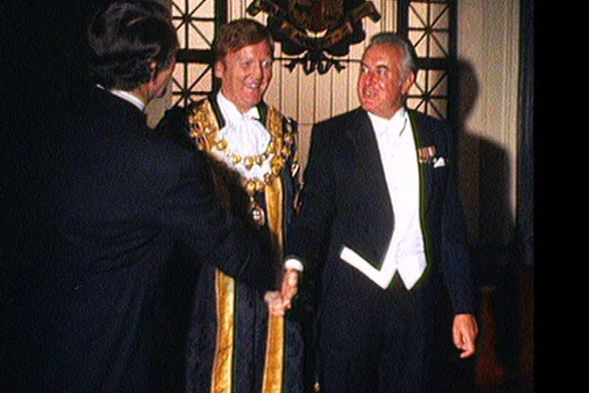 Ron Walker in his mayoral robes with men shaking hands.