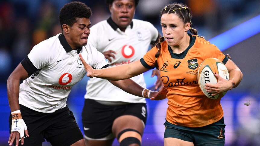 Desiree Miller holds the ball for the Wallaroos as she palms off a Fijiana opponent.