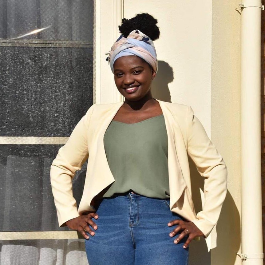 Portrait of Chanceline Kakule wearing a pastel blue and pink head wrap, along with a cream blazer, top and jeans.