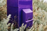 A purple bee hive with a purple box attached to the front.