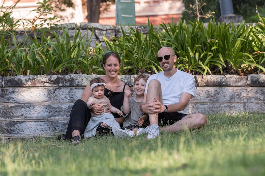 A young smiling couple with two young children sitting on a lawn