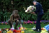 Two servicemen lay bouquets of flowers on the lawn outside Government House