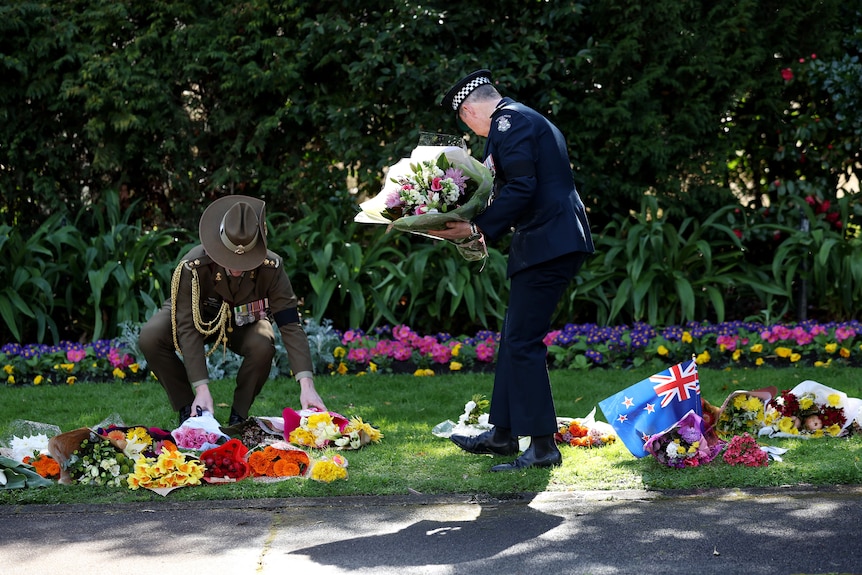 Two servicemen lay bouquets of flowers on the lawn outside Government House