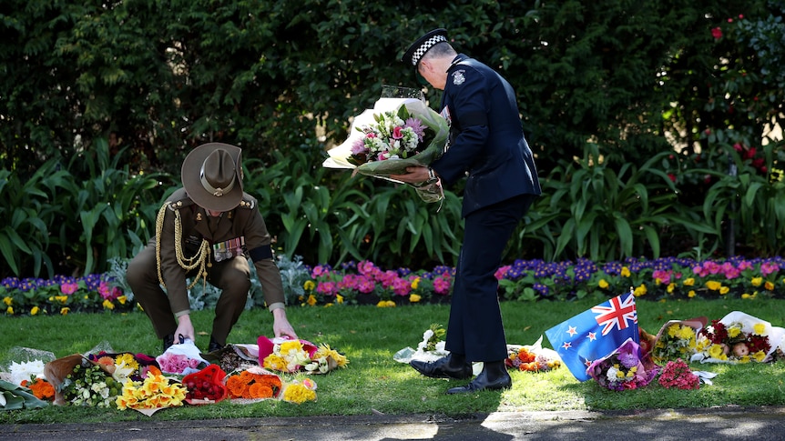 Two servicemen lay bouquets of flowers on the lawn outside Government House