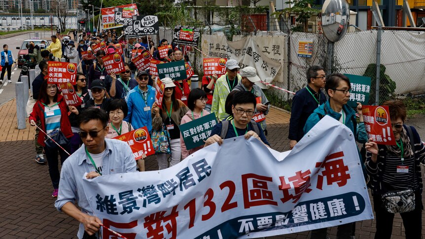 A group of Asian people hold banners with Chinese writing as they walk in a line on city street