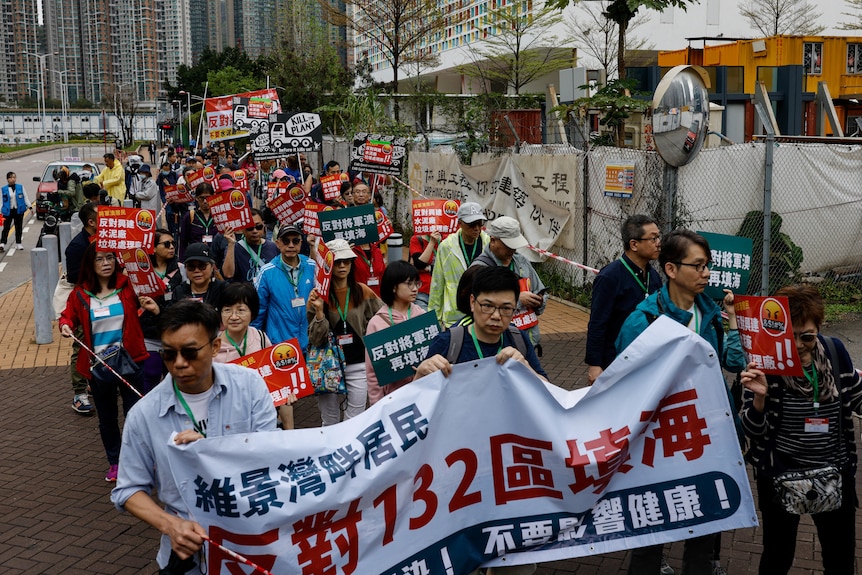 A group of Asian people hold banners with Chinese writing as they walk in a line on city street