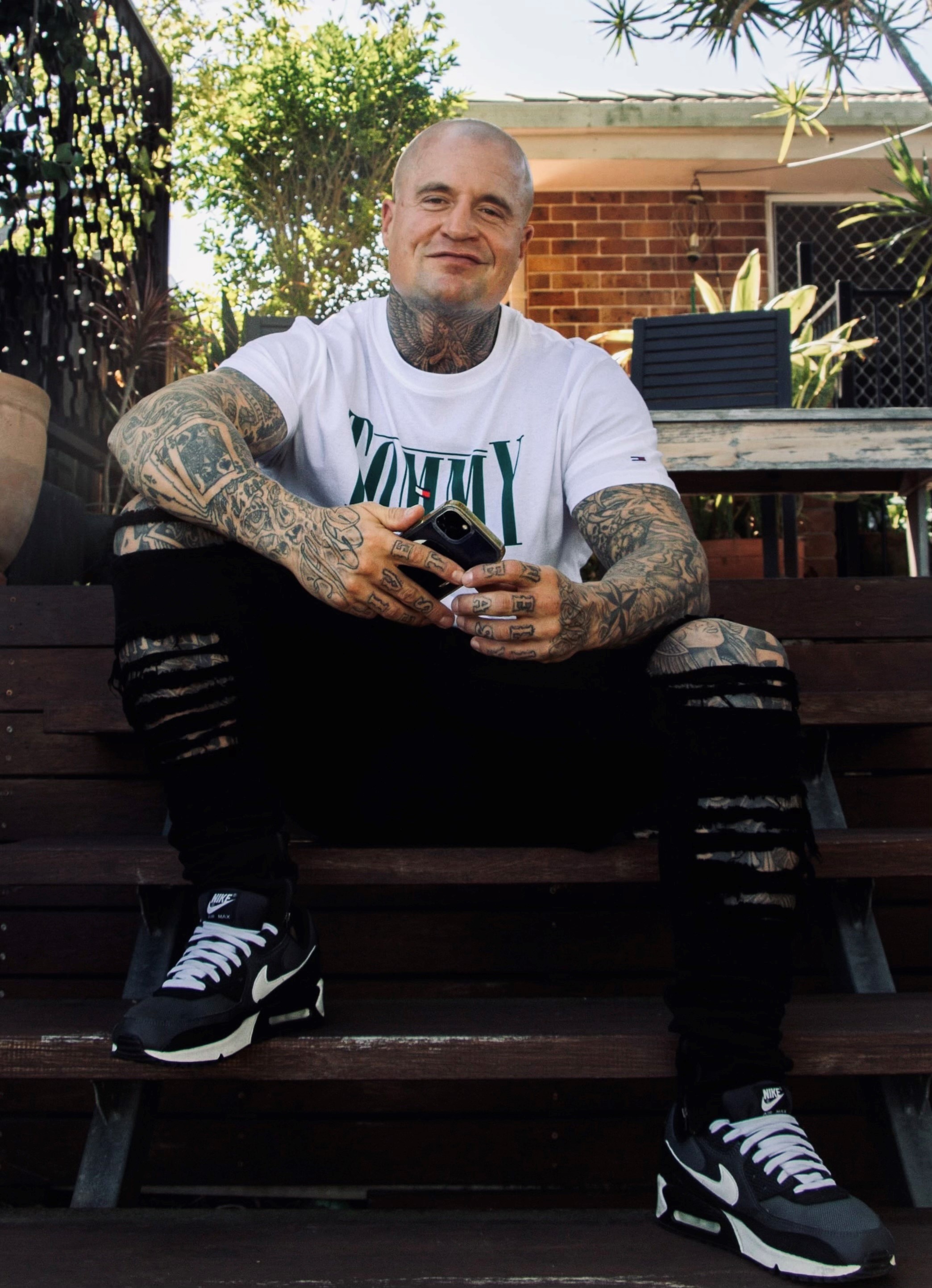 A man with tattoos on his neck and arms sits on a step