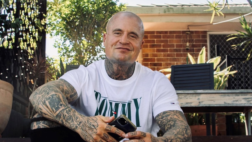 A man with tattoos on his neck and arms sits on a step