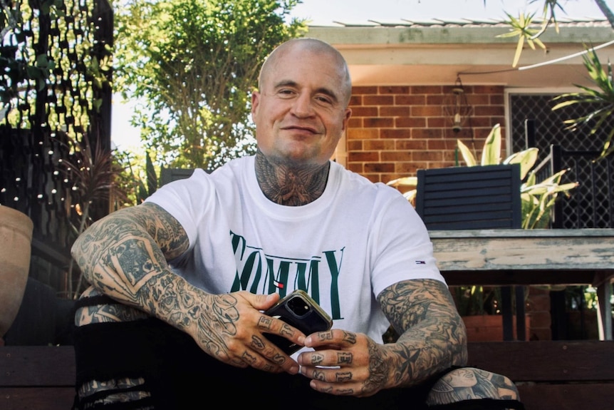 A man with tattoos on his neck and arms sits on a step