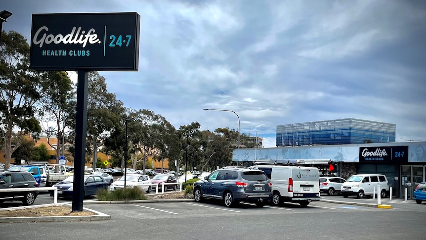 A carpark and building with a tall black sign saying Goodlife Health Clubs