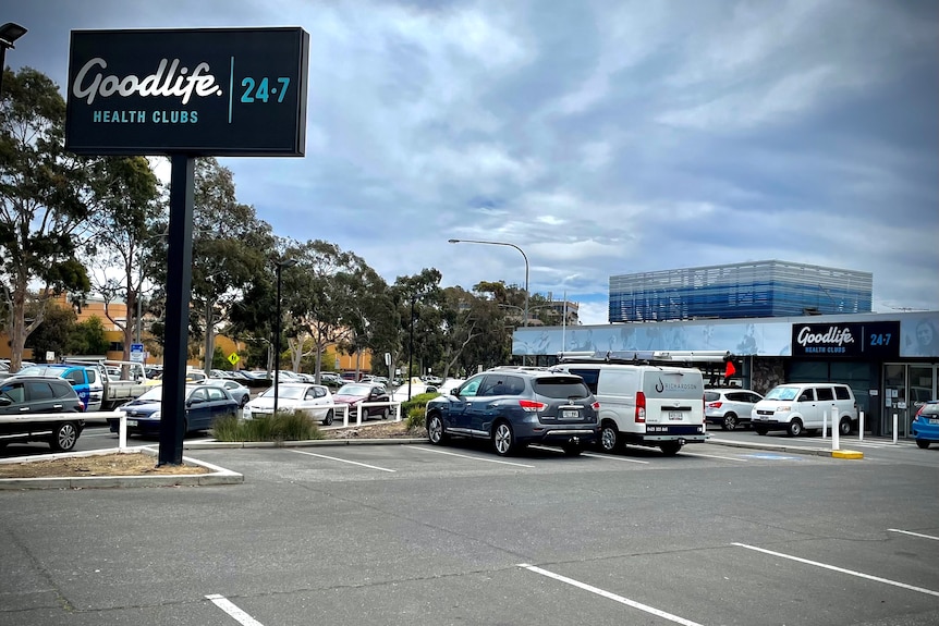 A carpark and building with a tall black sign saying Goodlife Health Clubs