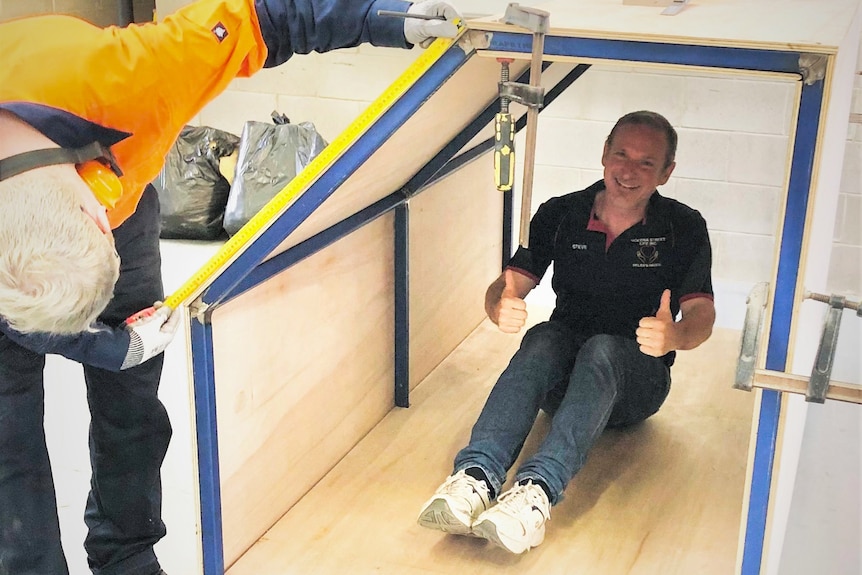 Man sitting inside a small wooden struture.