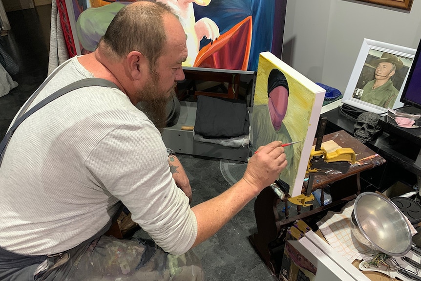 Mid shot of a man sitting in front of a canvas and painting a solider.