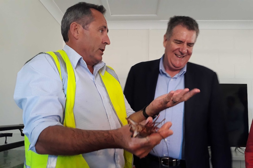 A man holds uncooked prawns in his hands while another man looks on